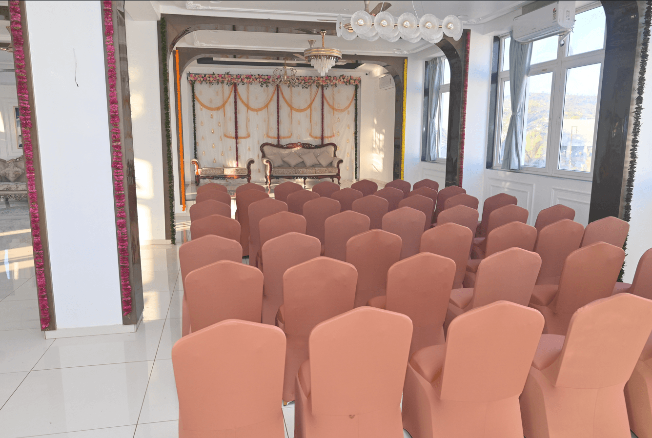 Indoor banquet hall laid out theatre-style with rows of covered chairs facing a decorated stage