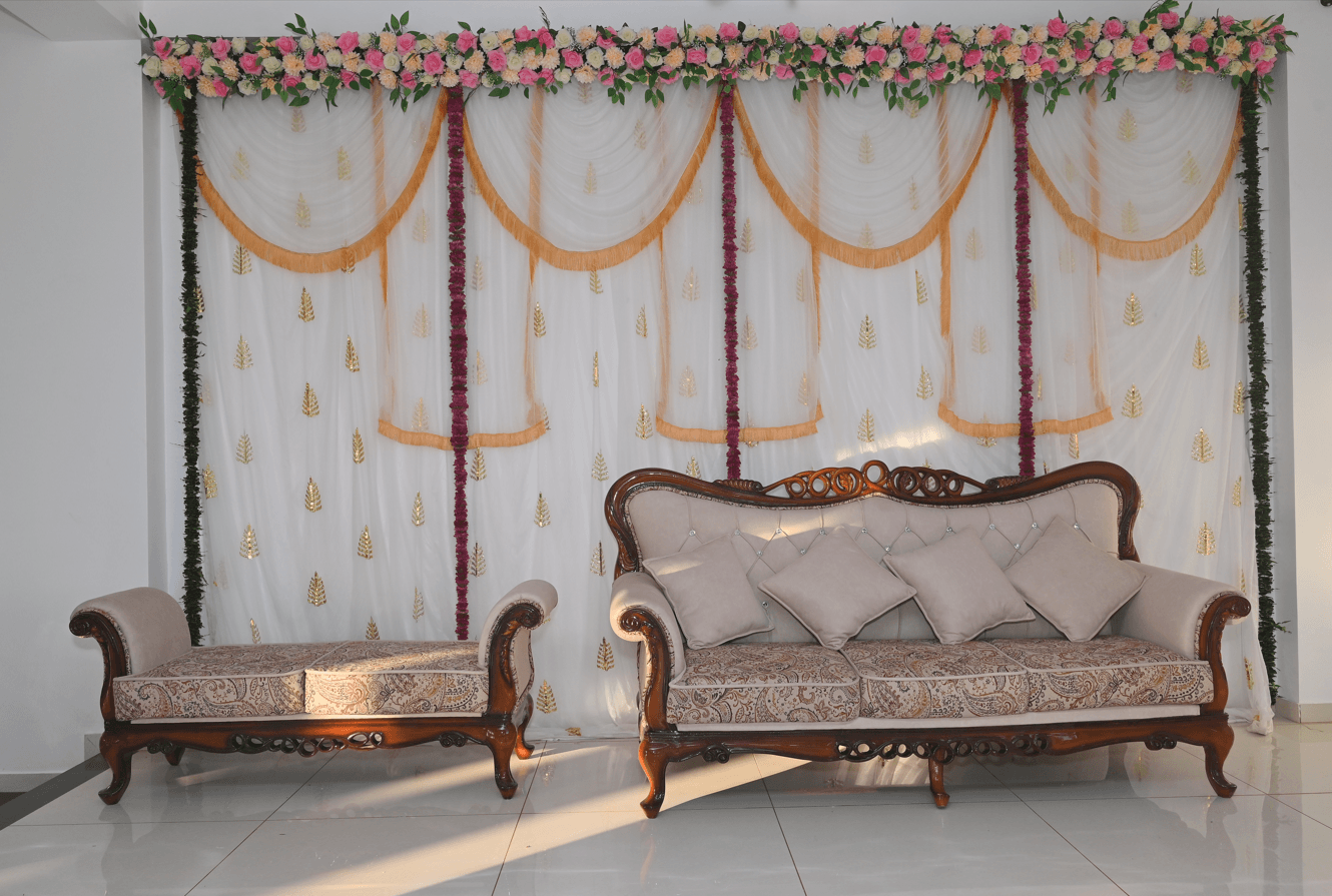 Banquet stage dressed with a draped backdrop, floral garland valance and a carved sofa set for the couple