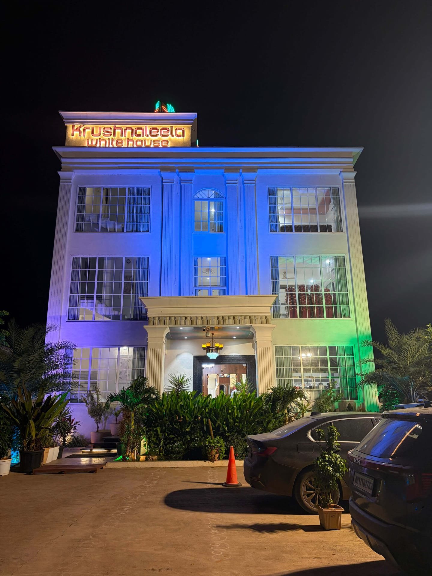 Front elevation of the hotel at night, tall grid windows glowing and palms framing the portico
