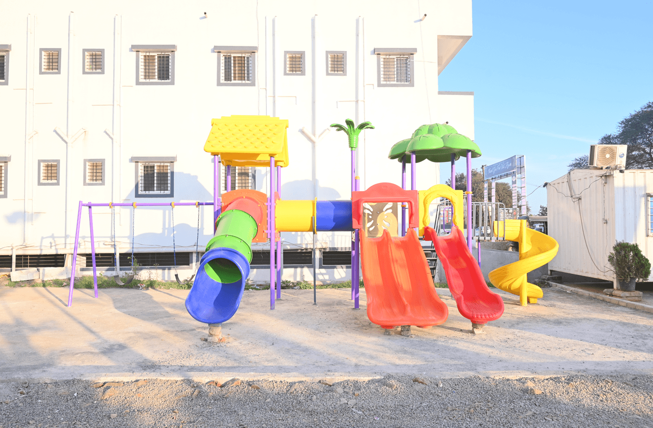 Outdoor children's play structure with slides, a climbing tunnel and swings beside the hotel building