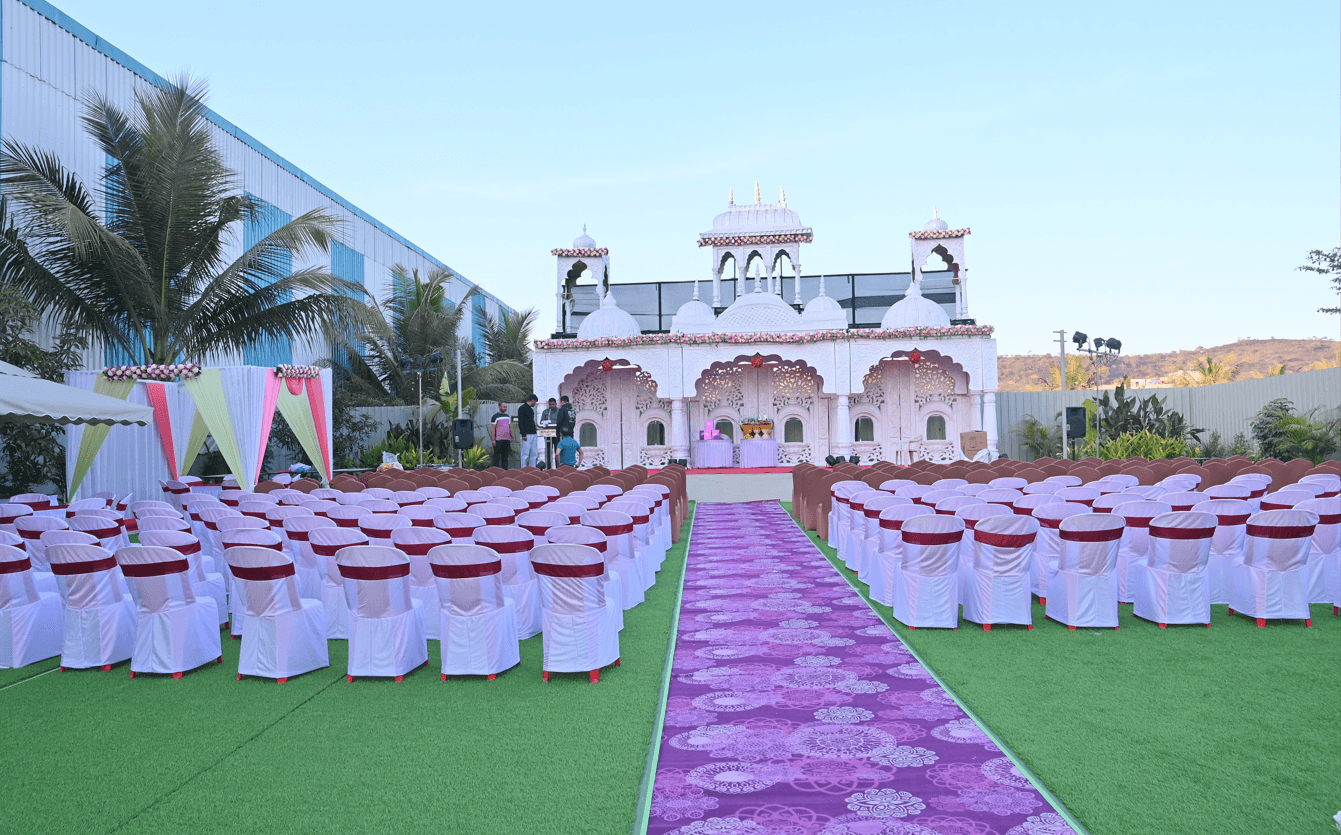 Wide view of the lawn venue with hundreds of covered chairs either side of a patterned aisle leading to the white mandap