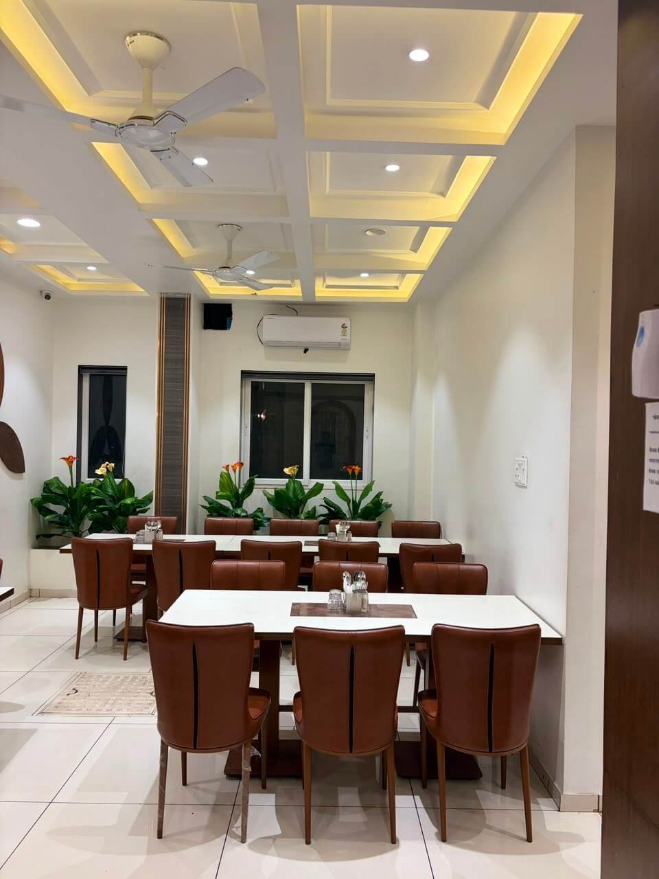 The pure vegetarian restaurant — coffered ceiling with warm cove lighting, long marble-topped tables, tan leather chairs and planters of calla lilies beneath the windows