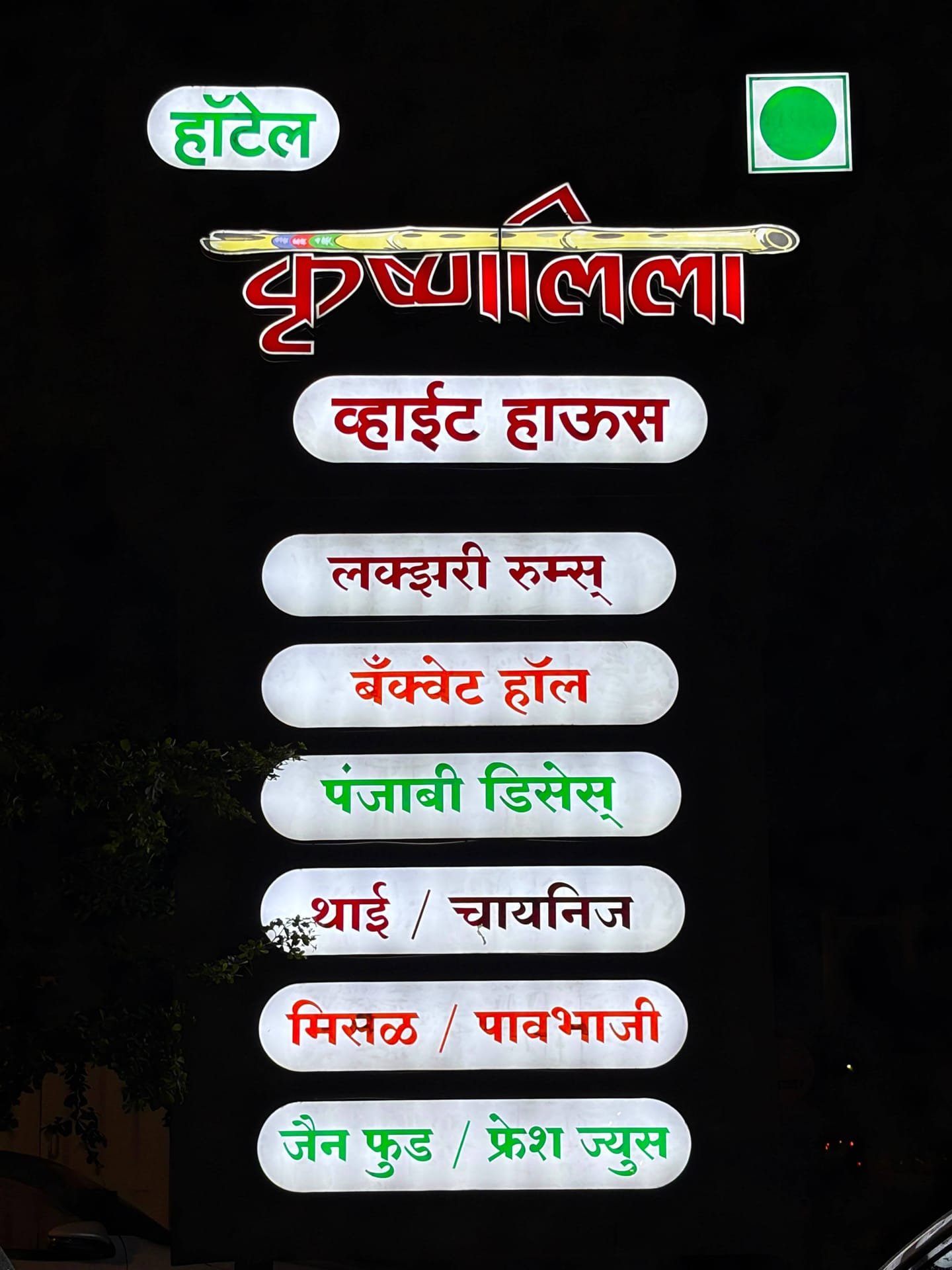 Illuminated Marathi signboard reading हॉटेल कृष्णालीला व्हाईट हाऊस, listing luxury rooms, banquet hall, Punjabi, Thai and Chinese dishes, misal, pav bhaji, Jain food and fresh juice, with the green pure-vegetarian mark